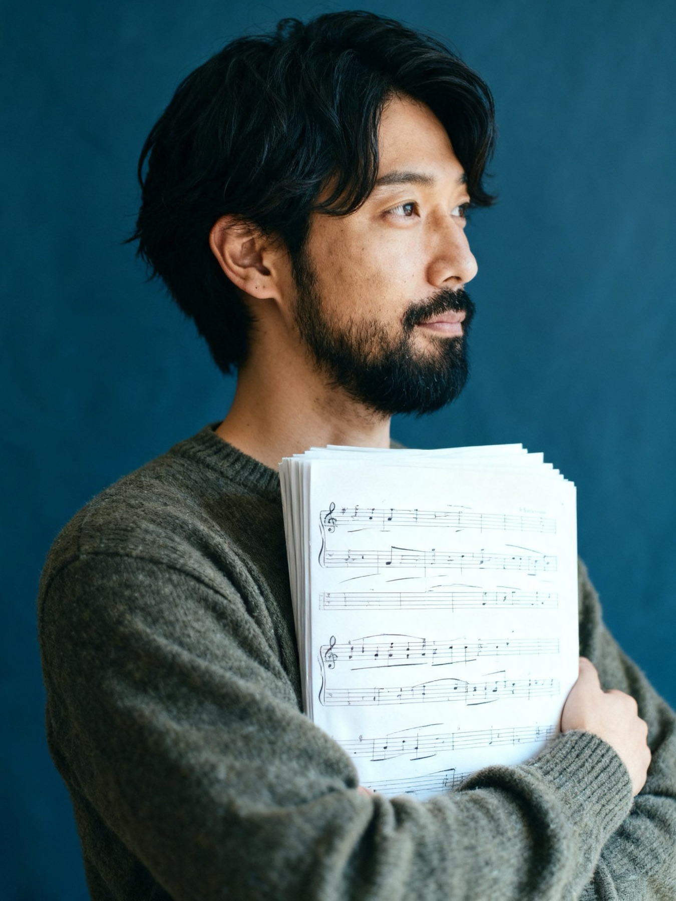 作曲家・30代男性。楽譜の束を抱えて横を向く（イメージ・架空の人物）
