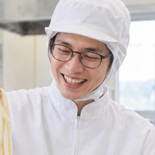 試作室でゆでた麺をざるで持ち上げる商品開発の社員