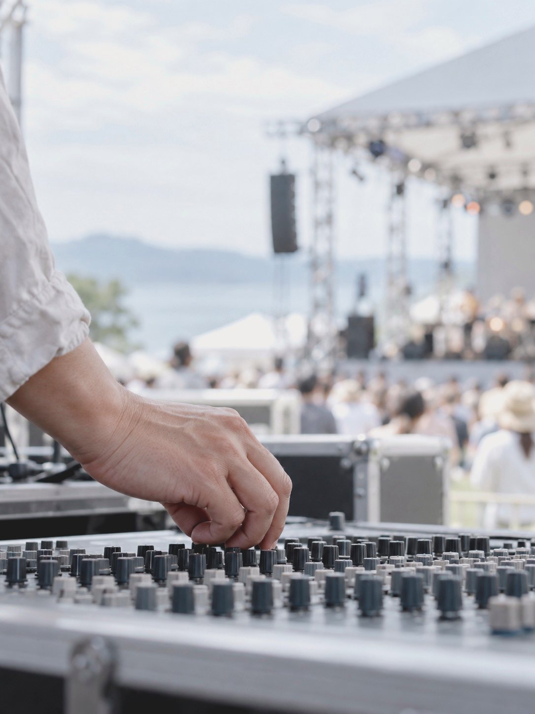 音響卓のつまみに置かれた手と、奥のステージ